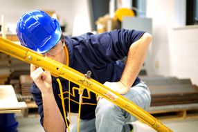 A male student in a blue hard hat inspects a piece of yellow steel.